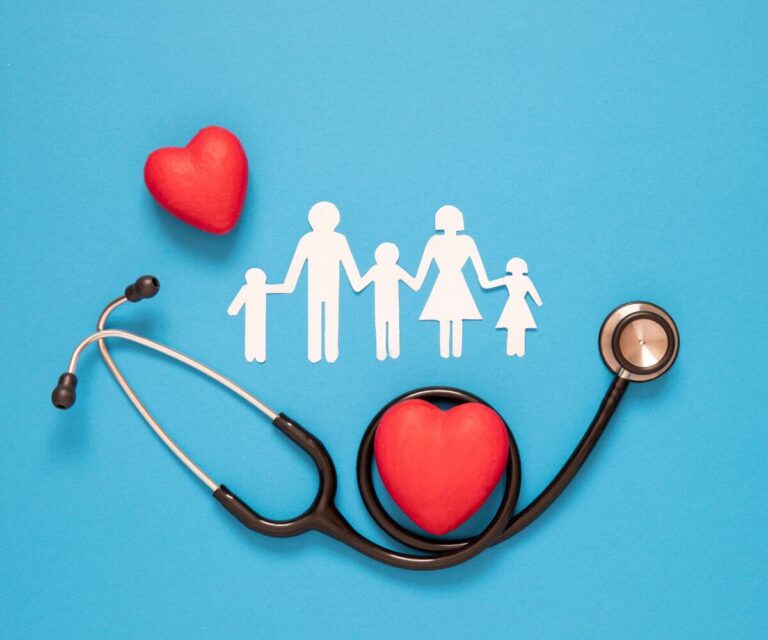 A stethoscope forms a circle around a red heart, with another heart nearby. Above them is a paper cutout of a family of four holding hands, all set against a blue background, symbolizing family health and care.