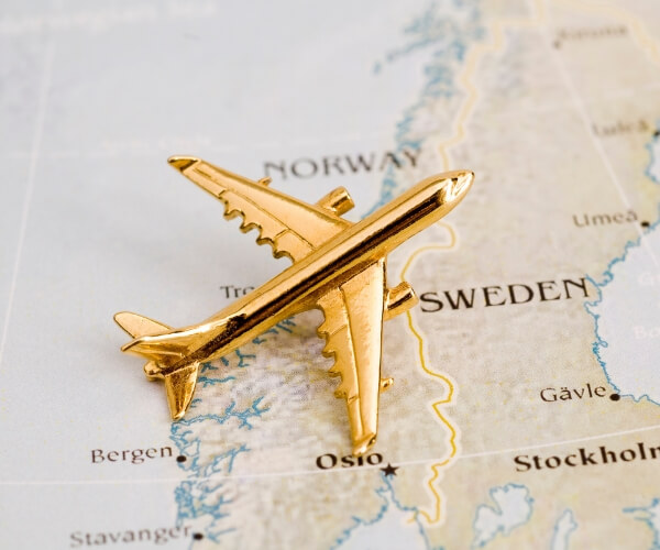A small gold airplane model rests on a map, positioned over Norway and Sweden near the city of Oslo, perhaps plotting a journey to compare surgery cost across Scandinavian countries.